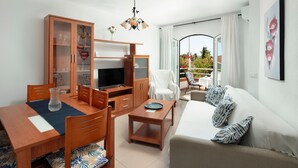 A modern living room with a sofa, TV, wooden cabinet, dining table, and chairs. - Apartment 'M - 1' with Shared Pool, Private Terrace and Wi-Fi (Torrox costa)