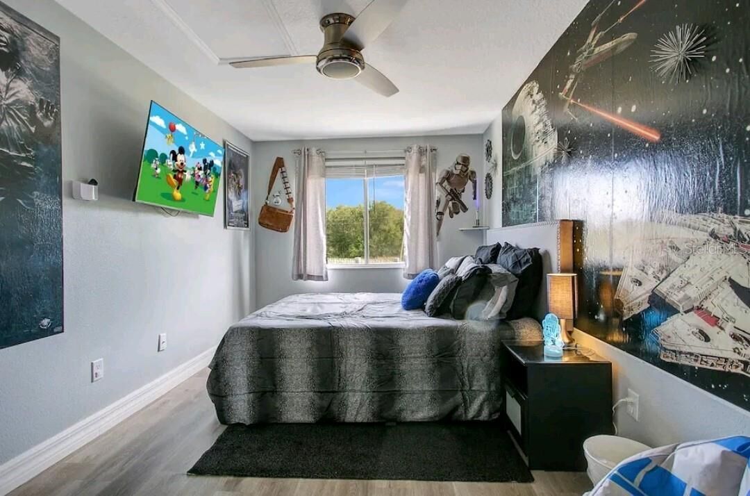 Ein Schlafzimmer mit einem Bett, einem Deckenventilator, einem Fenster mit Vorhängen und einer Wand mit Wandmalerei zum Thema Weltraum.