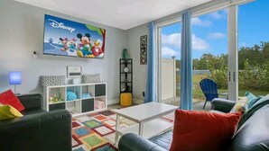 A living room with a large Disney-themed TV, a white coffee table, black leather sofas, and a colorful rug.