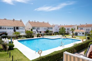 Une piscine entourée de bâtiments blancs aux toits recouverts de tuiles rouges, un ciel bleu azur et une végétation luxuriante et bien entretenue.