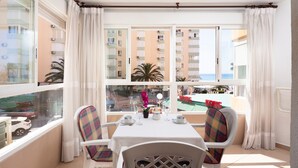 A balcony with a table set for two, chairs, and a view of a building and the sea. - Studio Apartment 'Estudio Bloque 89' with Sea View, Wi-Fi and Air Conditioning (Torrox)