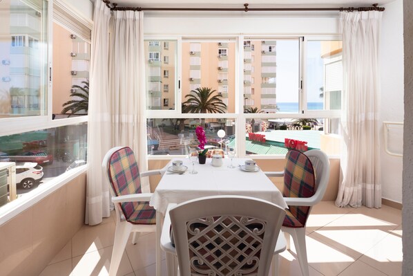Un balcon avec une table dressée pour deux personnes, des chaises et une vue sur un immeuble et la mer.
