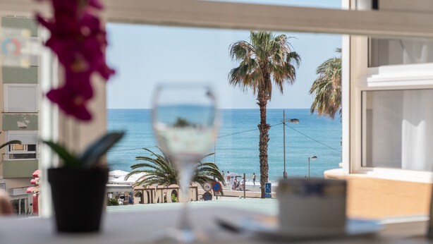 A view from a window overlooking a beach with palm trees, a glass of white wine, and a table with a potted plant. - Studio Apartment 'Estudio Bloque 89' with Sea View, Wi-Fi and Air Conditioning (Torrox)