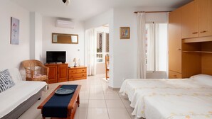 A bedroom with a bed, a sofa, a TV, a wooden cabinet, a wicker chair, and a window with curtains. - Studio Apartment 'Estudio Bloque 84' with Sea View, Wi-Fi and Air Conditioning (Torrox)