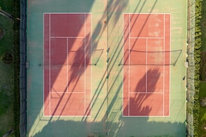 An aerial view of a tennis court with a net, surrounded by greenery.
