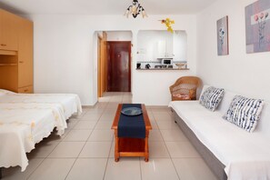 A room with two beds, a sofa, a small table, a mirror, and a kitchen area.