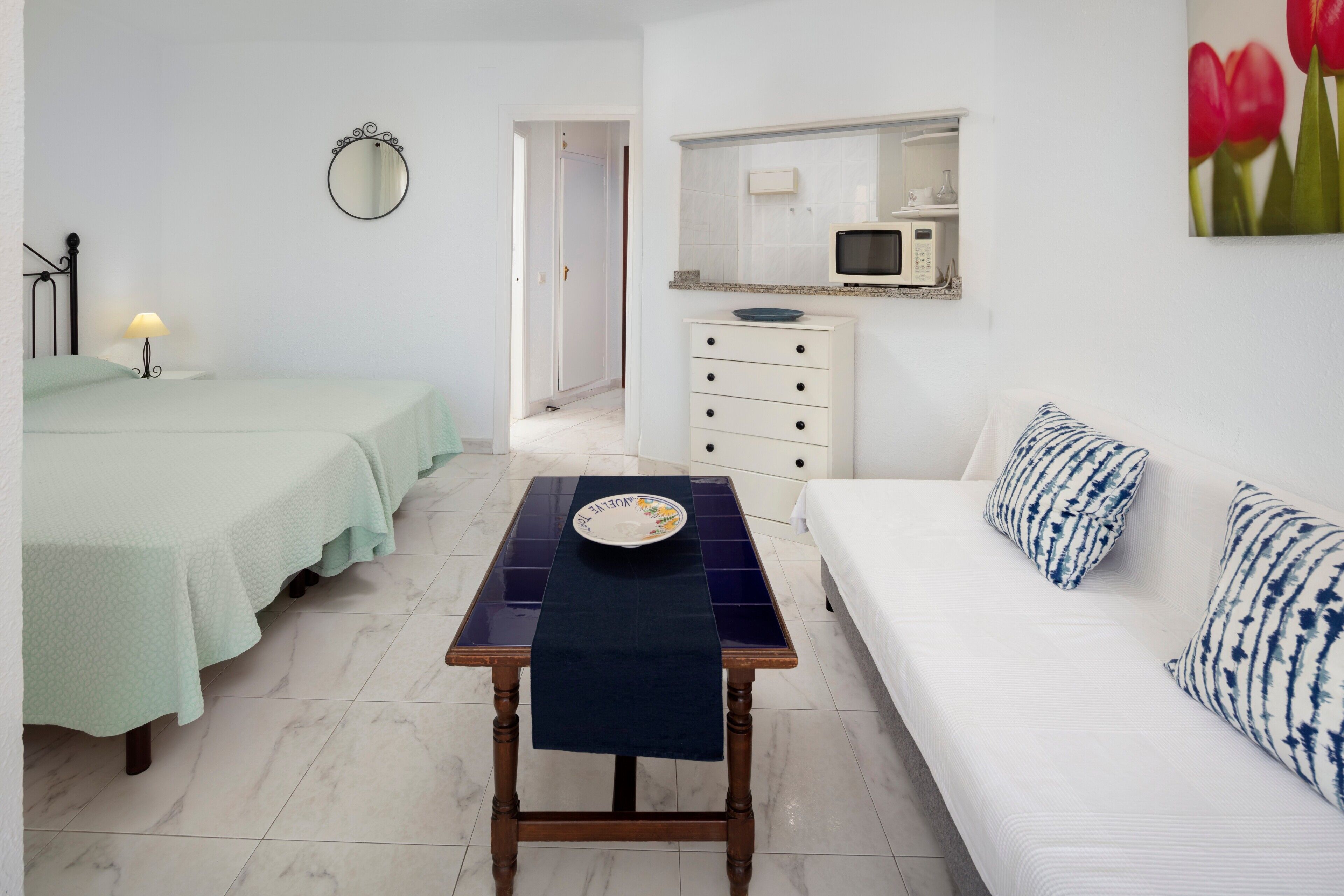 Une chambre à coucher avec un lit, une table avec une assiette, une commode, un four à micro-ondes et un miroir fixé au mur.