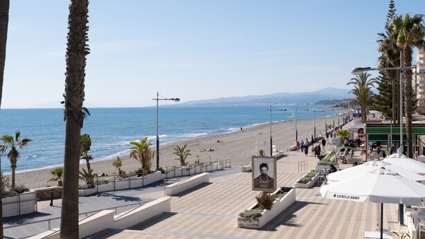 Une promenade en bord de mer, avec une plage, des palmiers et des espaces de détente en plein air.