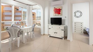 Un salon moderne comprenant un coin repas, un téléviseur à écran plat et un balcon offrant une vue sur les immeubles.