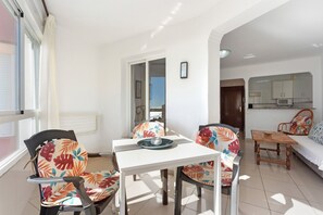 A dining area with a white table and chairs, a view of the outside, and a kitchen in the background. - Studio Apartment 'Estudio 07-11' with Sea View, Wi-Fi and Air Conditioning (Torrox)