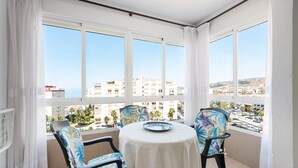 Un balcon avec une table et des chaises, de grandes fenêtres et une vue sur les immeubles et les palmiers.