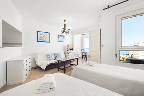 Hotellihuone, jossa on kaksi sänkyä, ruokapöytä, sohva, televisio ja ikkuna, josta on näkymä.