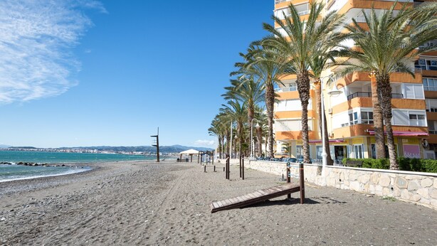 Une plage avec une promenade en bois, des palmiers et un immeuble à plusieurs étages doté de balcons.