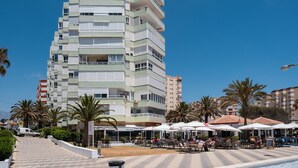 A multi-story hotel with balconies, outdoor seating, palm trees, and a clear blue sky.