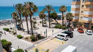 A coastal hotel with a parking area, palm trees, and a view of the sea.