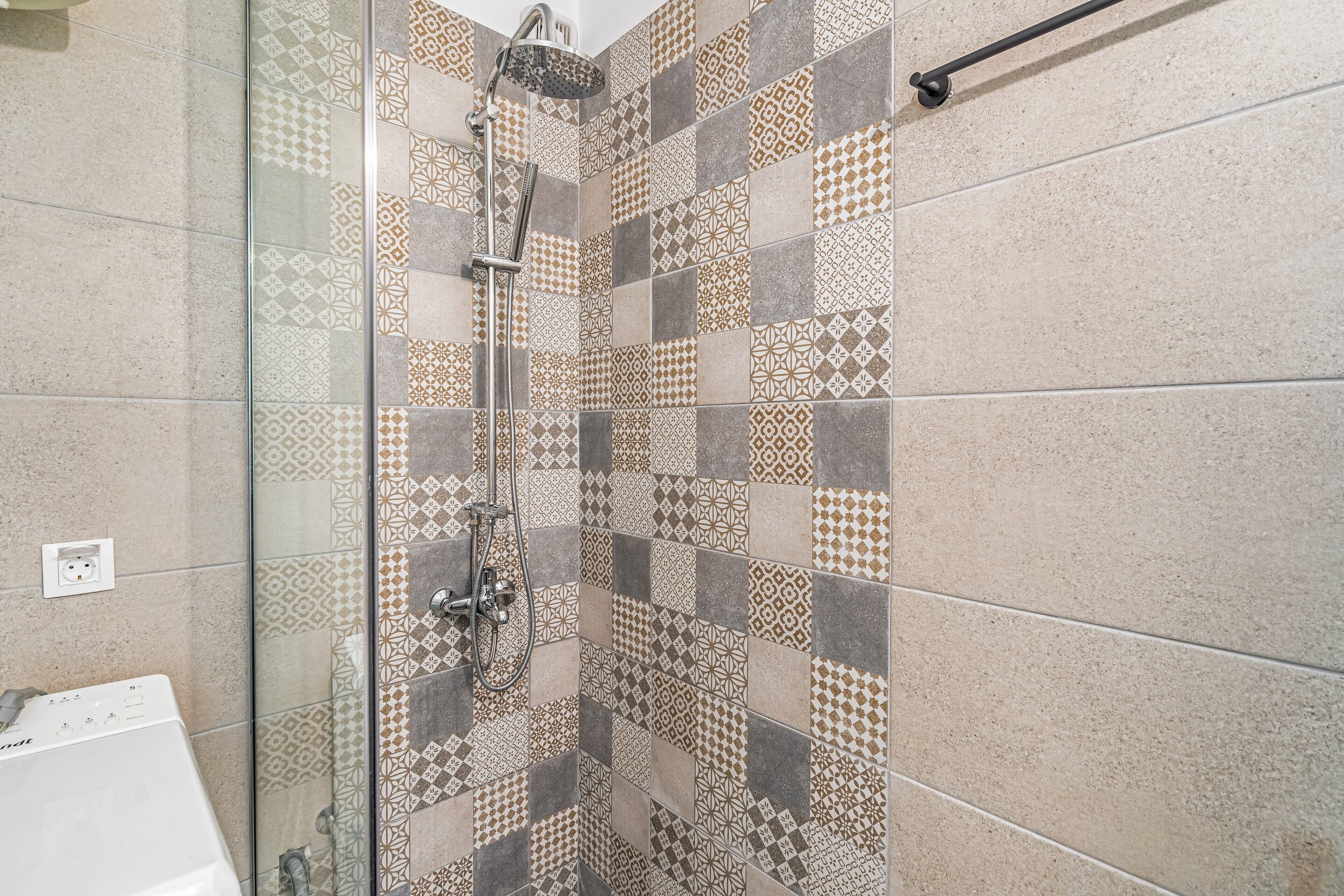 Un baño con ducha, separador de vidrio y baldosas estampadas.
