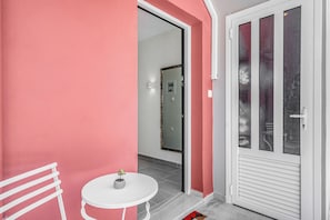 A room with a pink wall, a white door with frosted glass panels, a small round table with a potted plant, and a white chair.