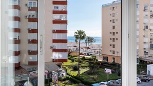 Un edificio de gran altura con varios balcones, un jardín bien cuidado con palmeras y vistas al mar.