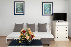 A bedroom with a bed, a dresser, a TV, and two framed floral paintings on the wall.