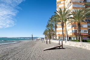 A beach with a wooden walkway, palm trees, and a multi-story building with balconies. - Studio Apartment 'Estudio 07-05' with Sea View, Wi-Fi and Air Conditioning (Torrox)