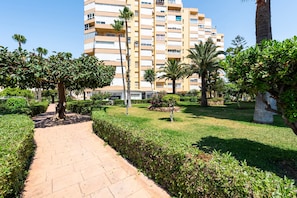 A pathway leading to a building with multiple floors, surrounded by well-maintained greenery and palm trees.