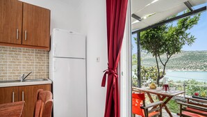 A compact kitchen with a refrigerator, wooden cabinets, and a red curtain. - Holiday Home 'Villa 2' with Sea View, Wi-Fi and Air Conditioning (Leykada)