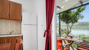 A kitchen with wooden cabinets and a white refrigerator, a dining area with a table and chairs, and a view of a body of water and hills. - Holiday Home 'Chakalaka - Villa 1' with Sea View, Wi-Fi and Air Conditioning (Leykada)
