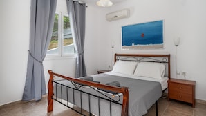 A bedroom with a bed, nightstand, and window with curtains. - Holiday Home 'Chakalaka - Villa 1' with Sea View, Wi-Fi and Air Conditioning (Leykada)