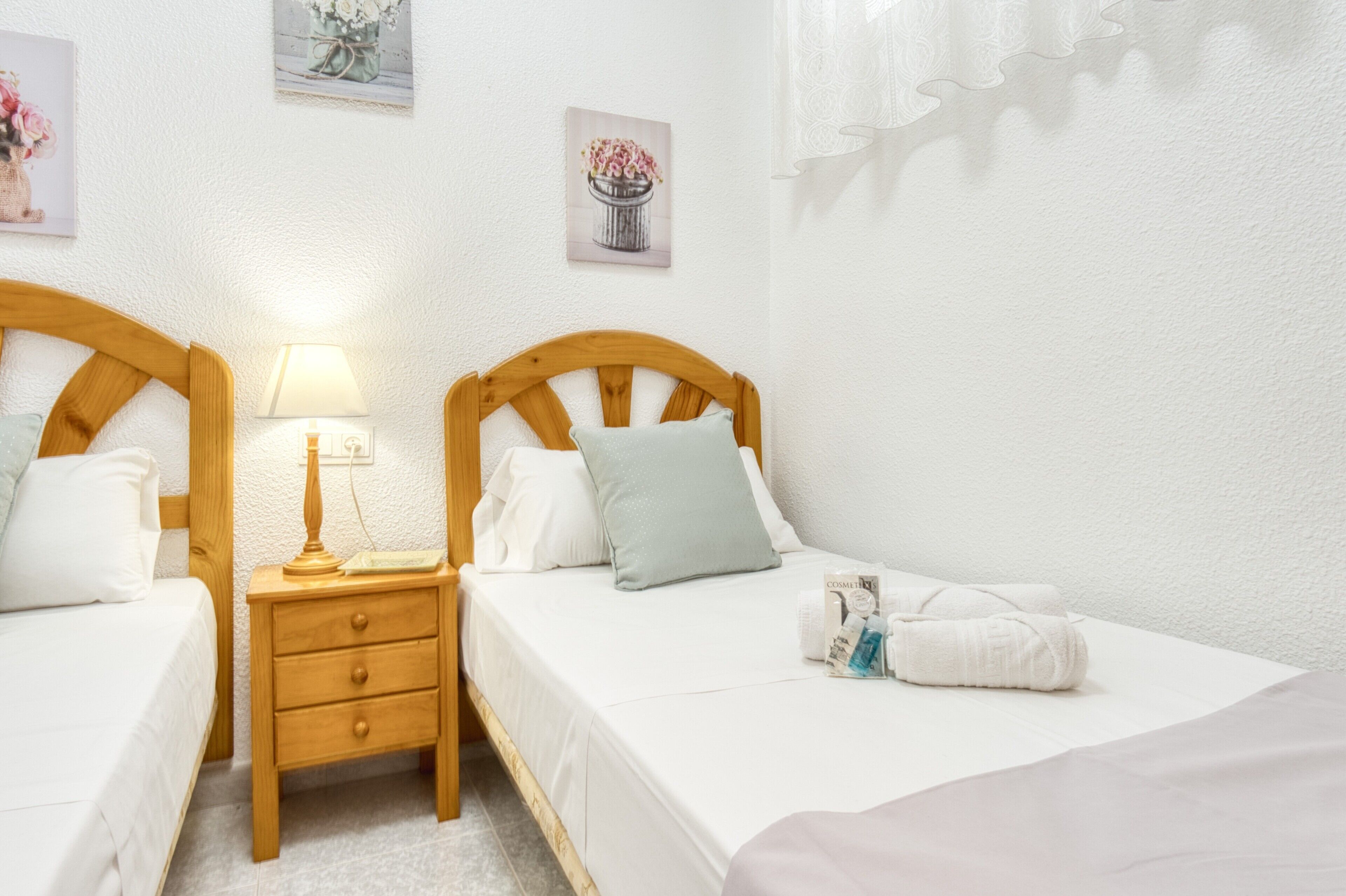 Une chambre avec deux lits, une table de chevet avec une lampe et une petite table avec des articles de toilette.