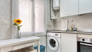 Una cocina moderna con lavadora integrada, estufa y ventana con cortina.