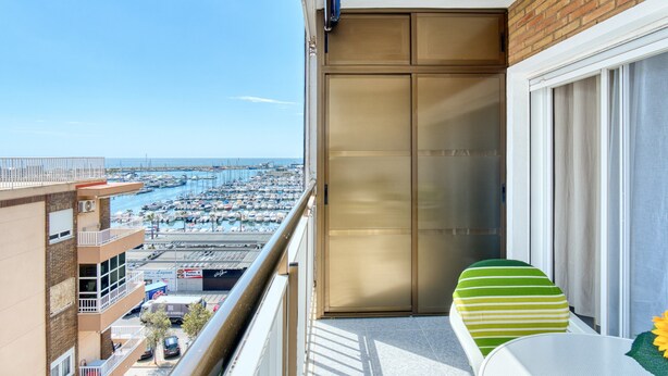 Un balcón con vista a un puerto deportivo y barcos, una puerta corredera, y una mesa con una silla.