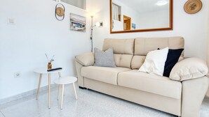 Una sala de estar moderna con un sofá color crema, una pequeña mesa redonda, una lámpara de pie y un espejo grande en la pared.