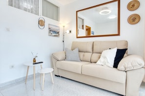 Una sala de estar moderna con un sofá color crema, una pequeña mesa redonda, una lámpara de pie y un espejo grande en la pared.