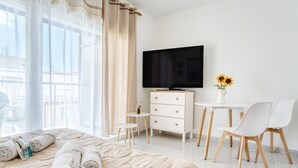 Habitación de hotel con cama, televisión, una pequeña mesa con sillas y un florero con flores.