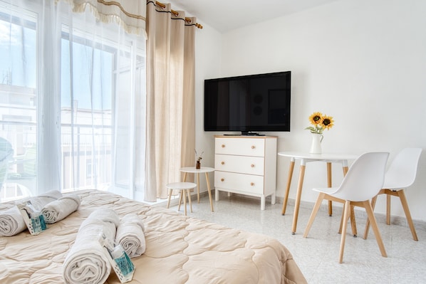 Habitación de hotel con cama, televisión, una pequeña mesa con sillas y un florero con flores.