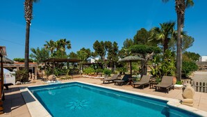 Une piscine avec des chaises longues, des palmiers et une pergola.