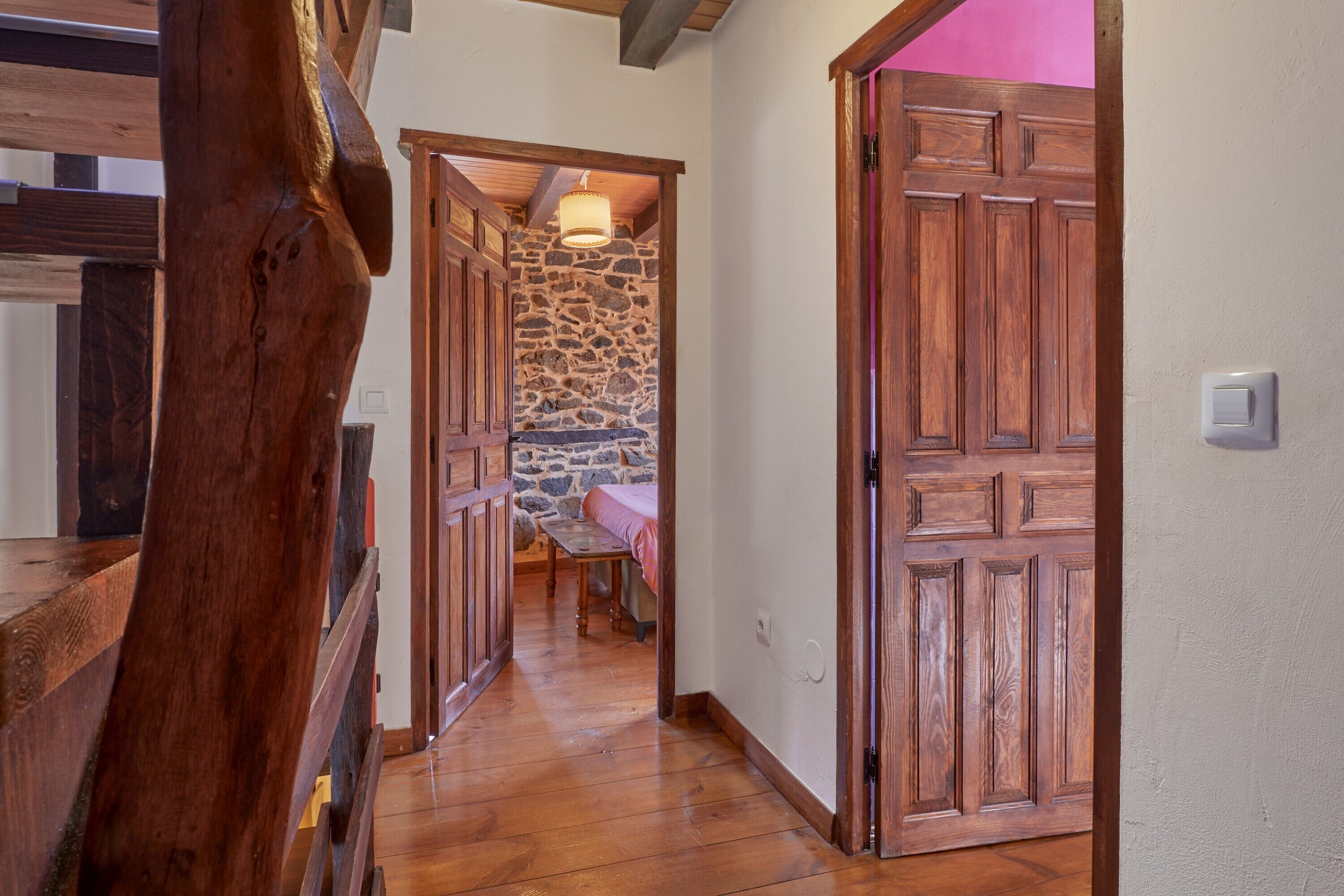 Una escalera de madera que lleva a una habitación con pared de piedra y una cama.