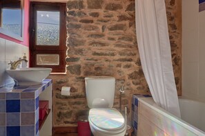 Ein Badezimmer mit Steinwand, Toilette, Waschbecken und Fenster.