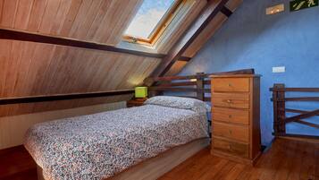 Un dormitorio con techo inclinado, una cama con colcha estampada, un aparador de madera y un tragaluz.
