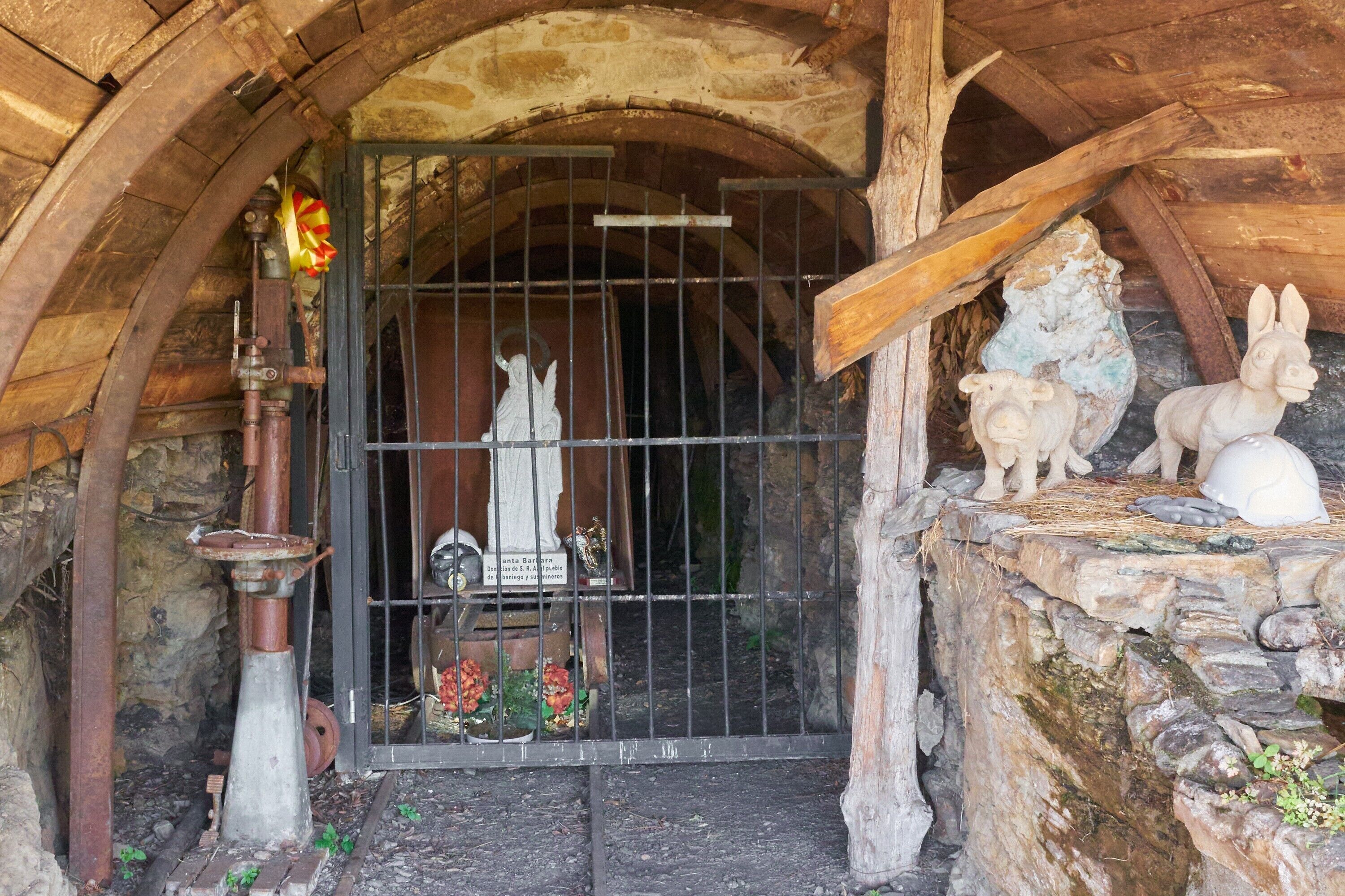 Un arc en pierre rustique mène à une porte en bois surmontée d’un portail en métal, le tout étant entouré de murs en pierre et agrémenté d’une corniche en pierre ornée de sculptures de lapins.