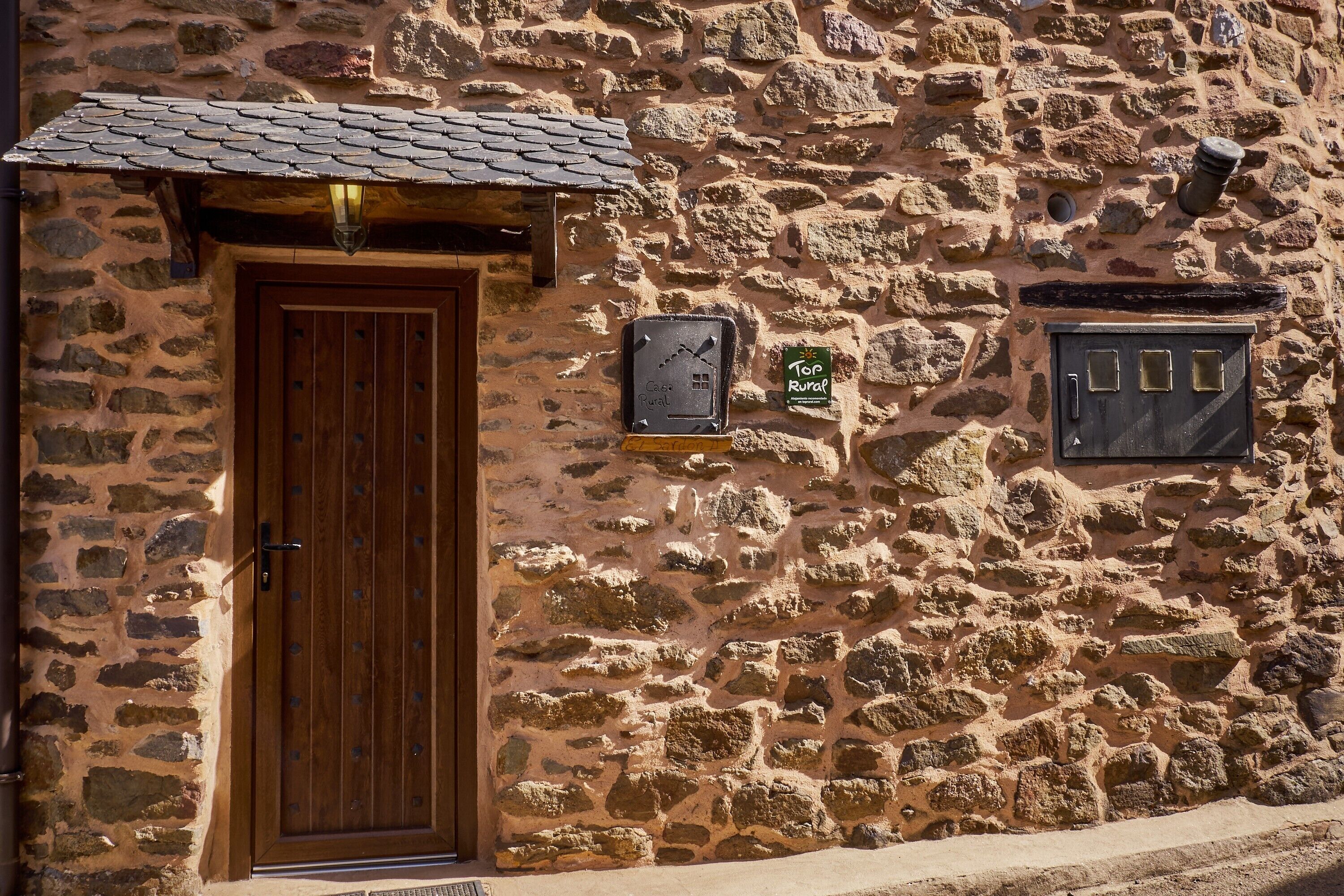 Un edificio de piedra con puerta de madera, una ventana pequeña y un cartel en la pared.