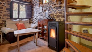 A cozy room with a stone wall, a wooden table, a sofa, a fireplace, and a window with shutters. - Country House 'El Sardón 2' with Mountain View, Wi-Fi and Air Conditioning (Labaniego)
