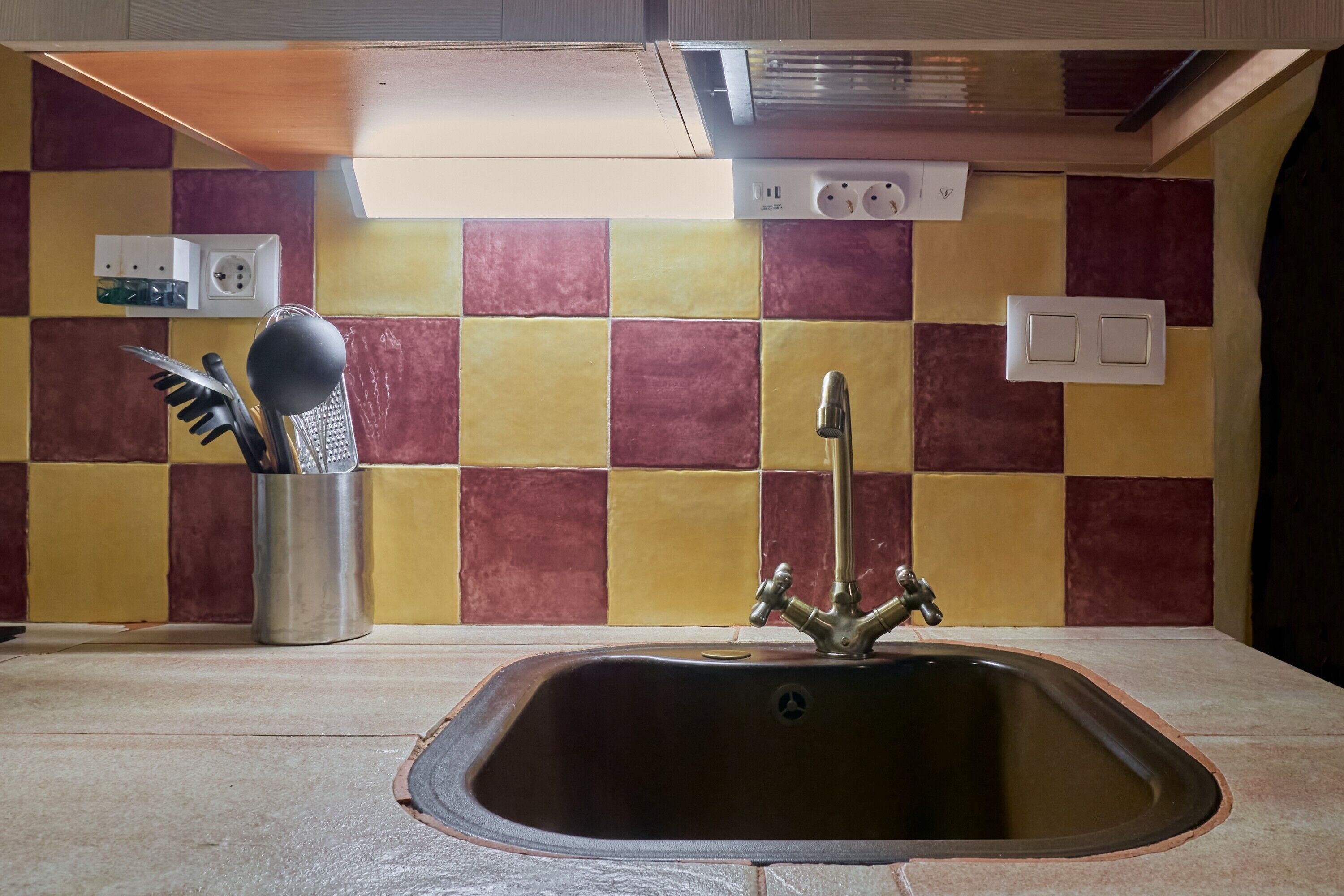 Una cocina con un lavamanos, un organizador de utensilios y un protector salpicadero de azulejos.