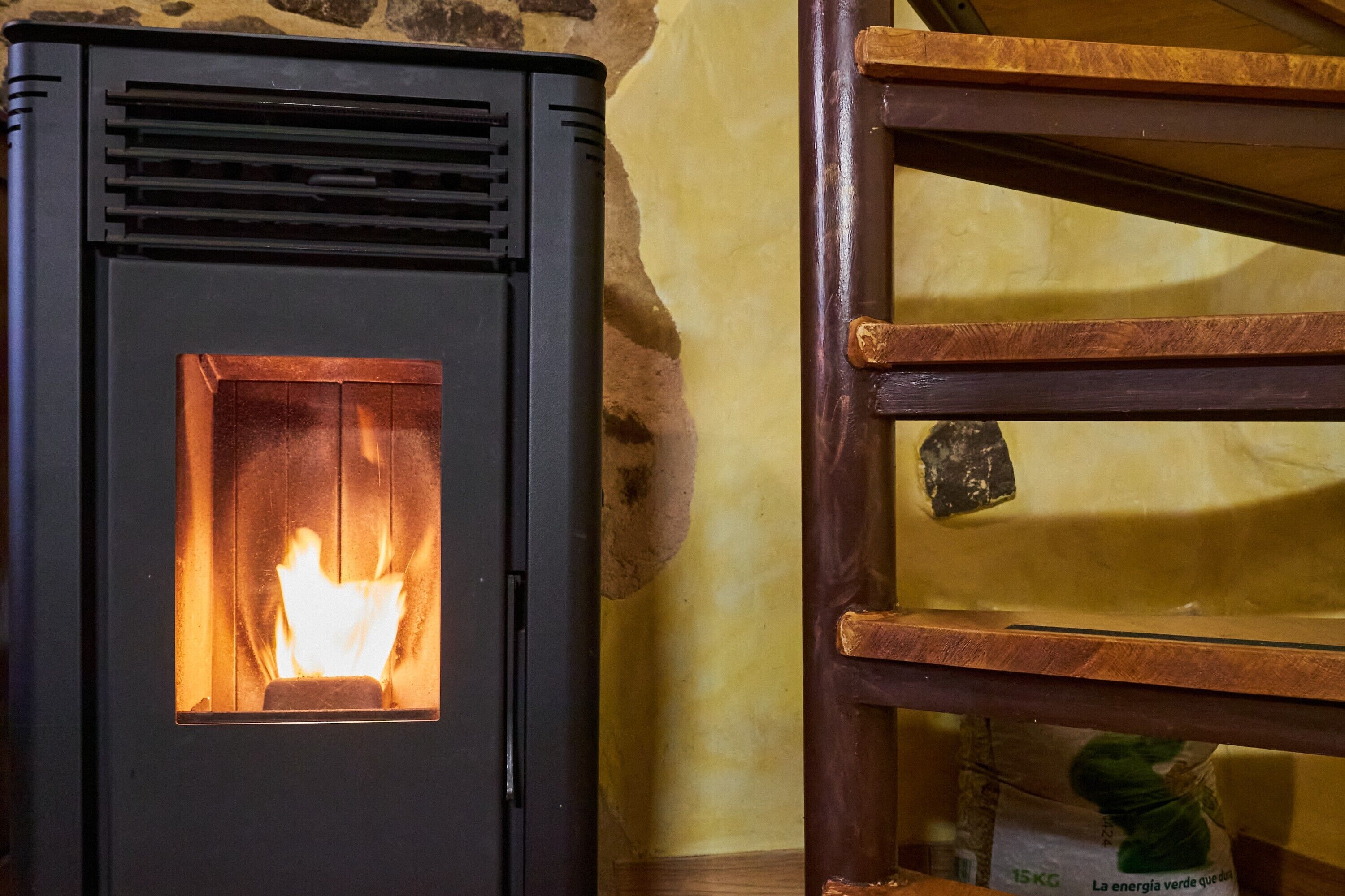 Un camino a legna con fuoco vivo, una sedia di legno e un muro in pietra.