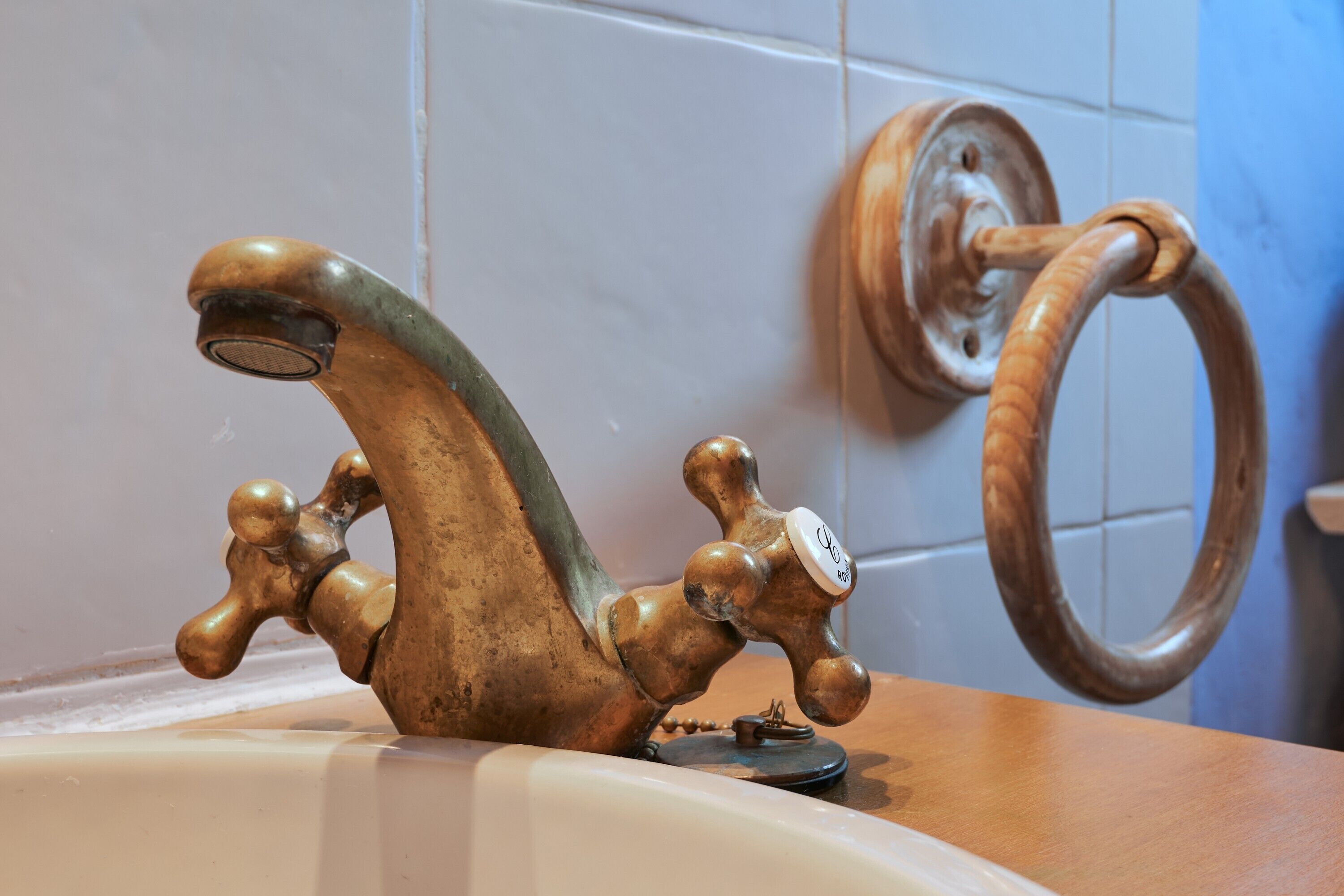 Een oude kranen van messing met een houten hendel, een houten ring en een witte betegelde muur.