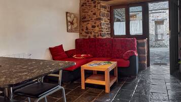 Una habitación acogedora con pared de piedra, sofá rojo estampado, una mesa de madera y una ventana con cortinas.
