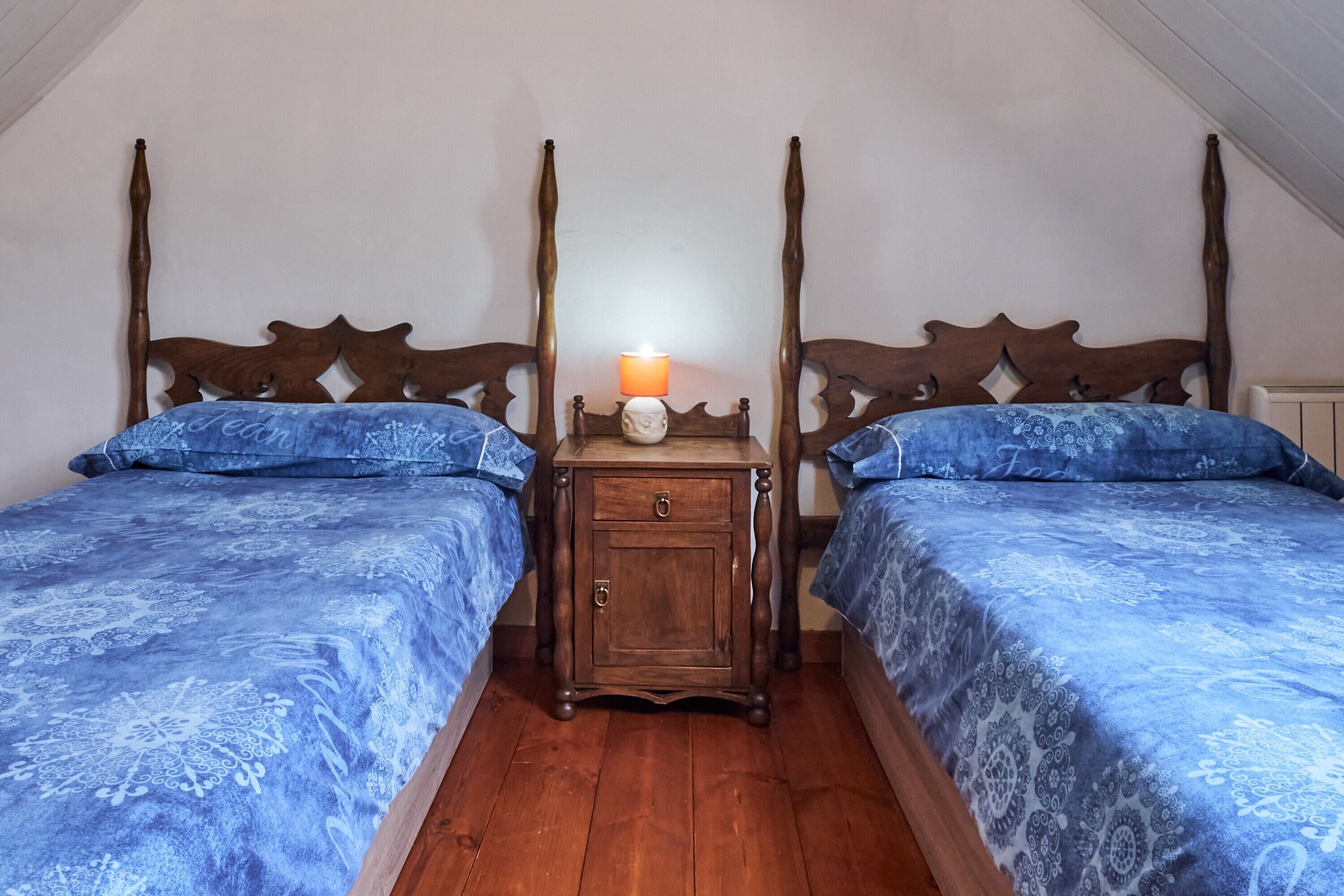 A bedroom with two beds, a nightstand with a lamp, and a wooden headboard.