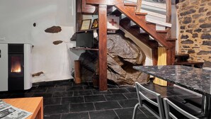 Een rustiek interieur met een stenen muur, een houten trap, een open haard en een eethoek met een tafel en stoelen.
