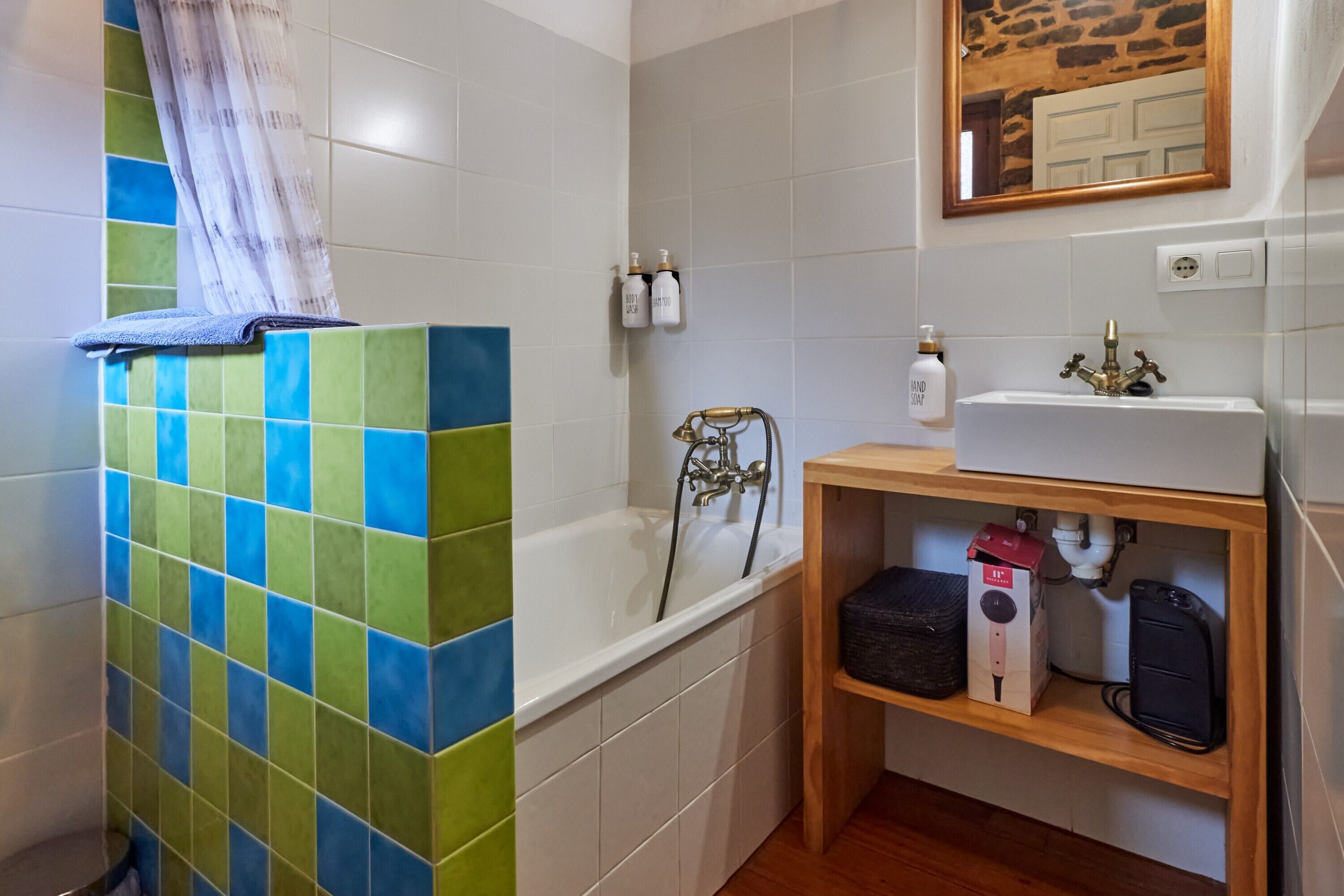 Un baño con ducha de azulejos, un lavamanos con espejo y un estante con artículos de aseo.