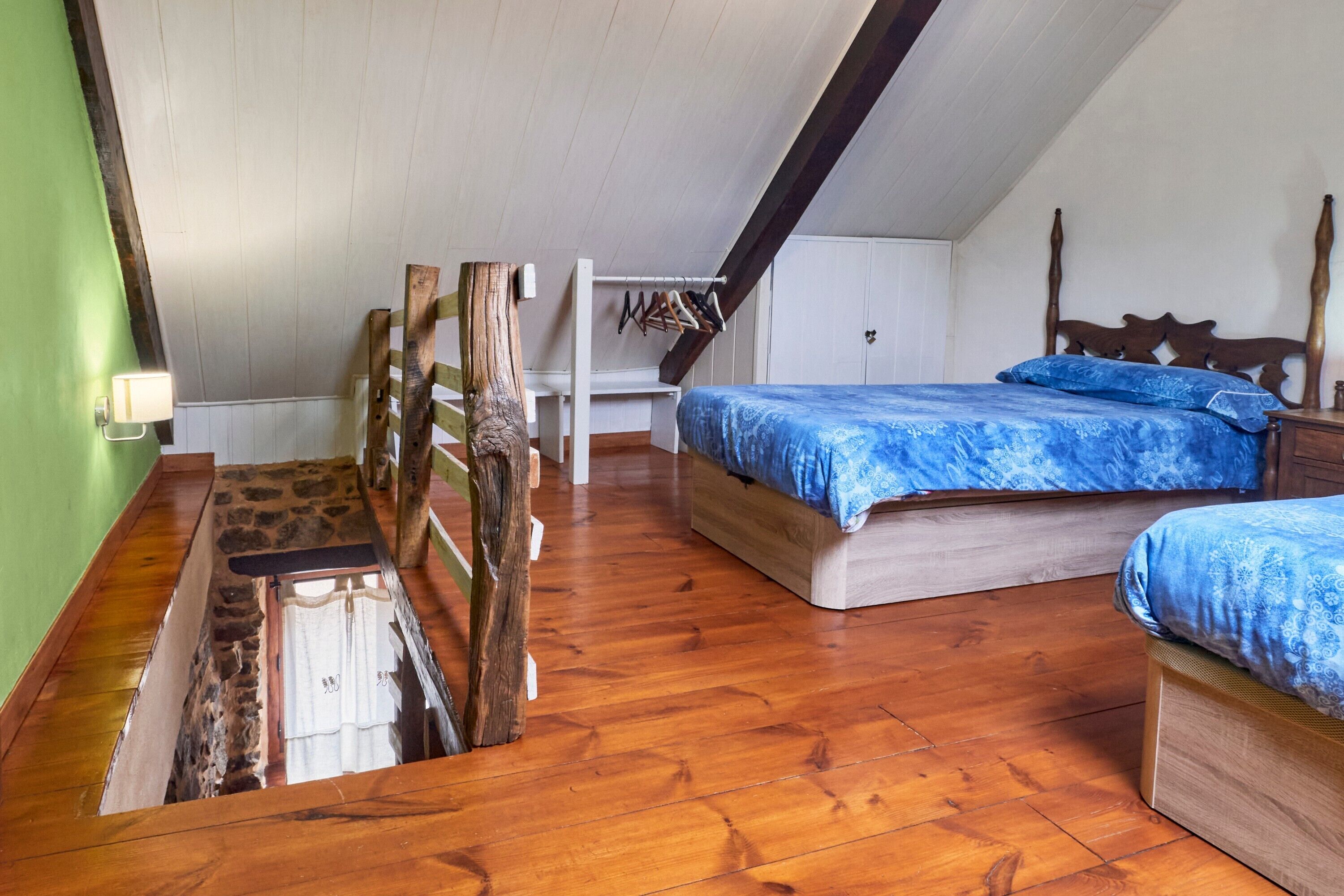 Une chambre avec un plafond en pente, un plancher en bois, un lit avec une literie bleue, une tête de lit en bois et une petite table de chevet.